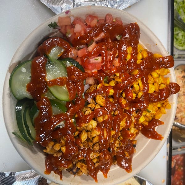 A Korean-Mexican bowl with chicken, corn, cucumbers, tomatoes, and a generous drizzle of red sauce.
