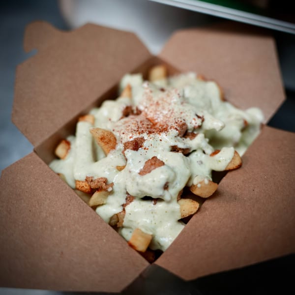 Korean-style fries topped with creamy white sauce and red seasoning in a brown takeout box.