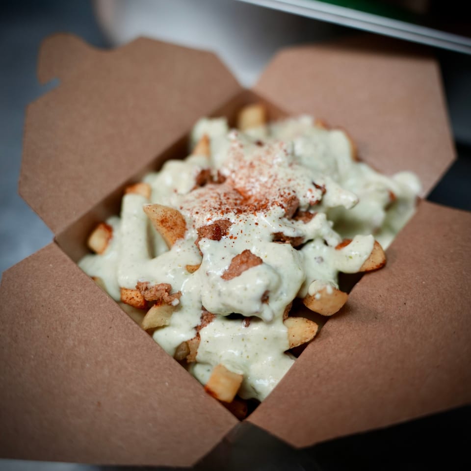 Korean-style fries topped with creamy white sauce and red seasoning in a brown takeout box.