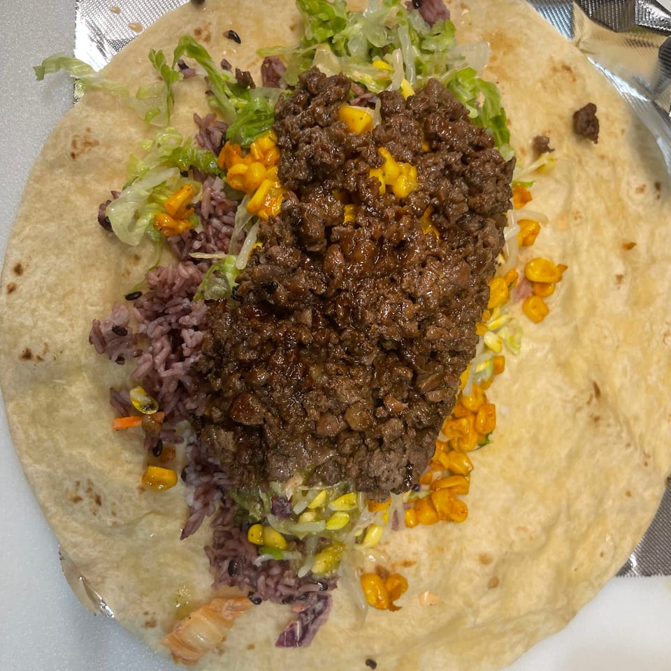 Overhead view of a Bebop Korean Mexican Grill burrito with ground beef, purple rice, corn, and lettuce.
