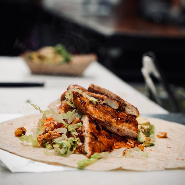 Steaming Korean grilled chicken, lettuce, and rice on a tortilla, ready to be wrapped.